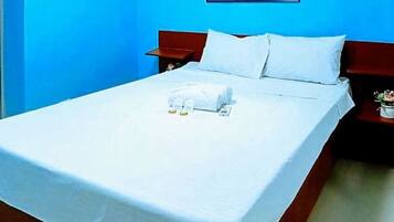 A hotel room with a bed, a nightstand, a small table with a plant, and a mirror on the wall.