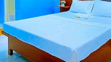 A bed with a white sheet, a wooden headboard, and a small bedside table with a vase of flowers.