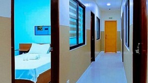 A hotel corridor with a bed in the foreground, a wooden door at the end, and a framed picture on the wall. - Jeanines Travellers Inn by RedDoorz (Morong)
