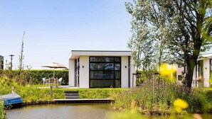 A modern house with a large window, a small garden, and a pond. - Modern Chalet With Dishwasher (Nieuwerkerk aan den IJssel)
