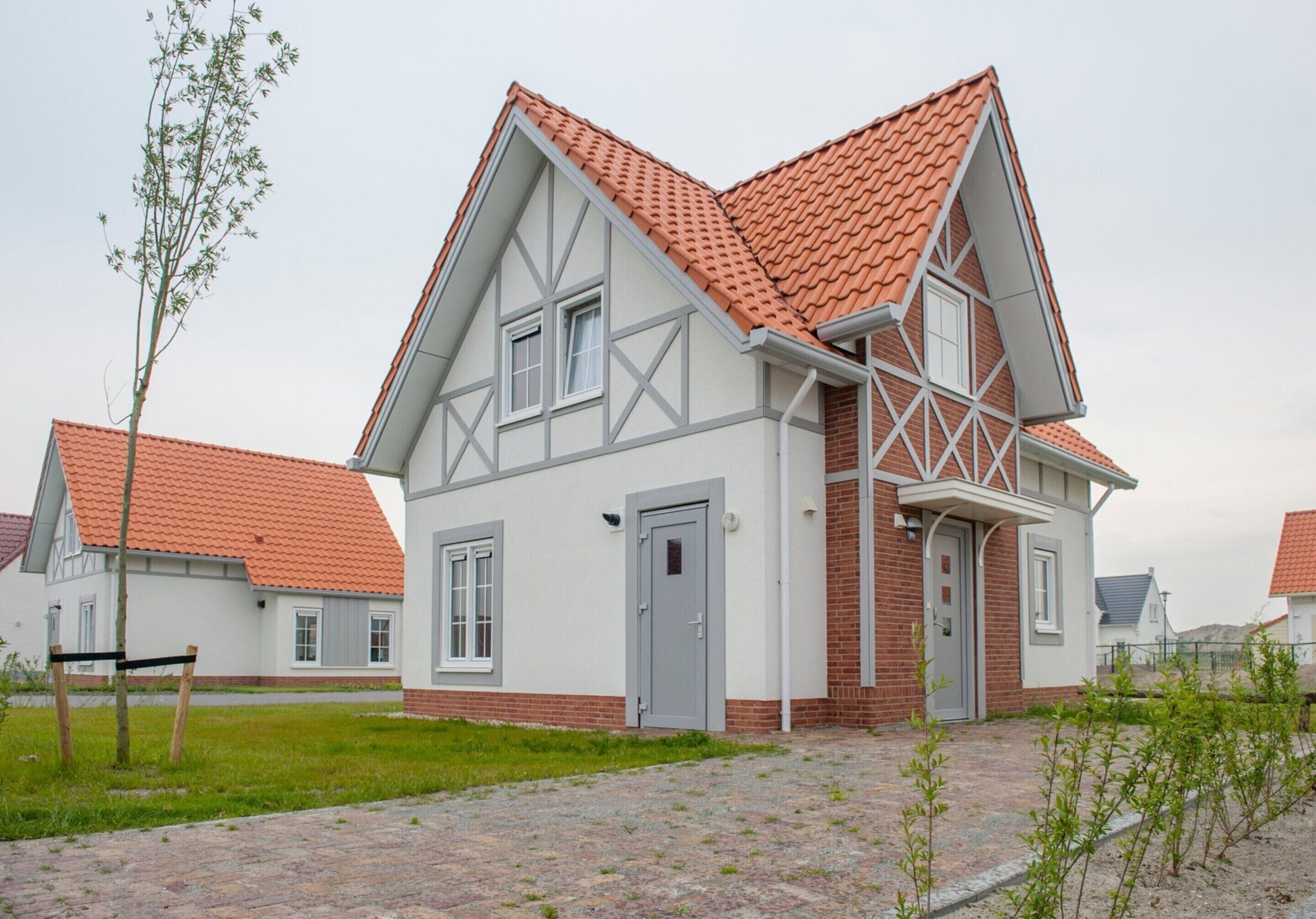 A two-story house with a red-tiled roof, white walls, and a brick section.
