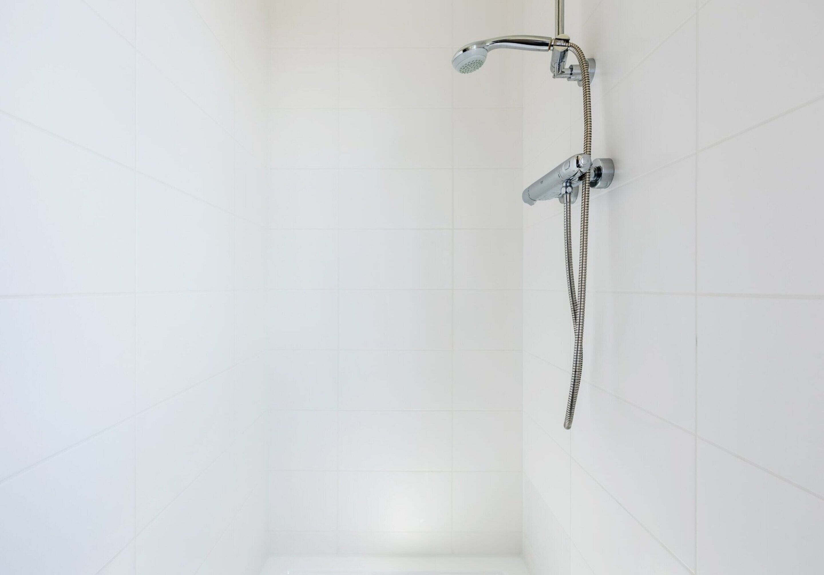 A shower with a handheld showerhead and a fixed wall-mounted showerhead, both with hoses.