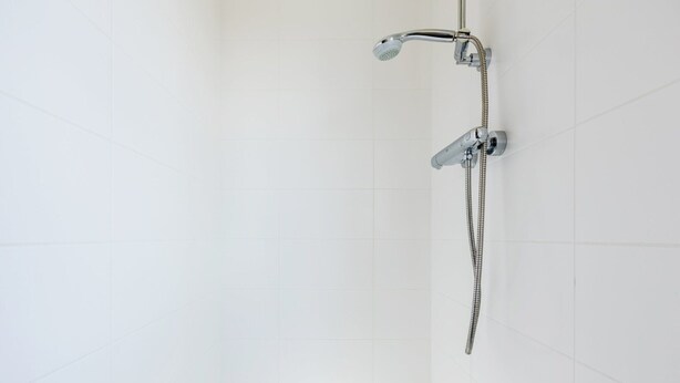 Een douche met een handdouche en een vaste douchekop aan de muur, beide met slangen.