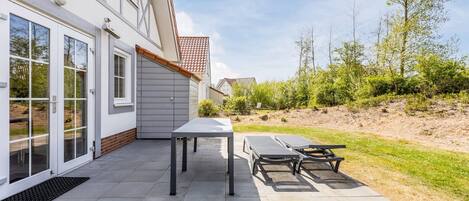 A modern building with a patio area featuring a table and two lounge chairs.