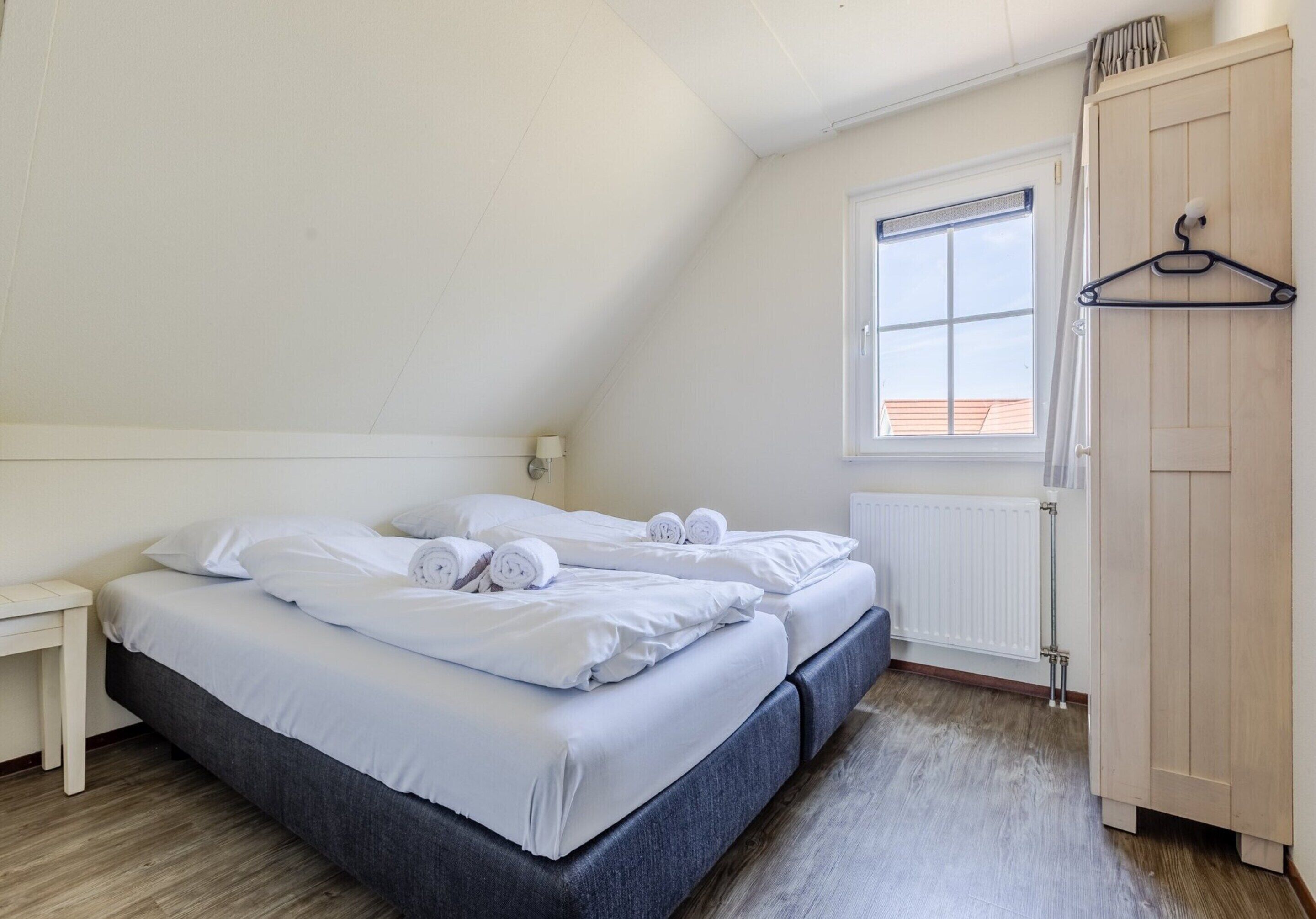 A bedroom with two beds, a wooden wardrobe, a window with blinds, and a radiator.