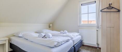 A bedroom with two beds, a wooden wardrobe, a window with blinds, and a radiator.