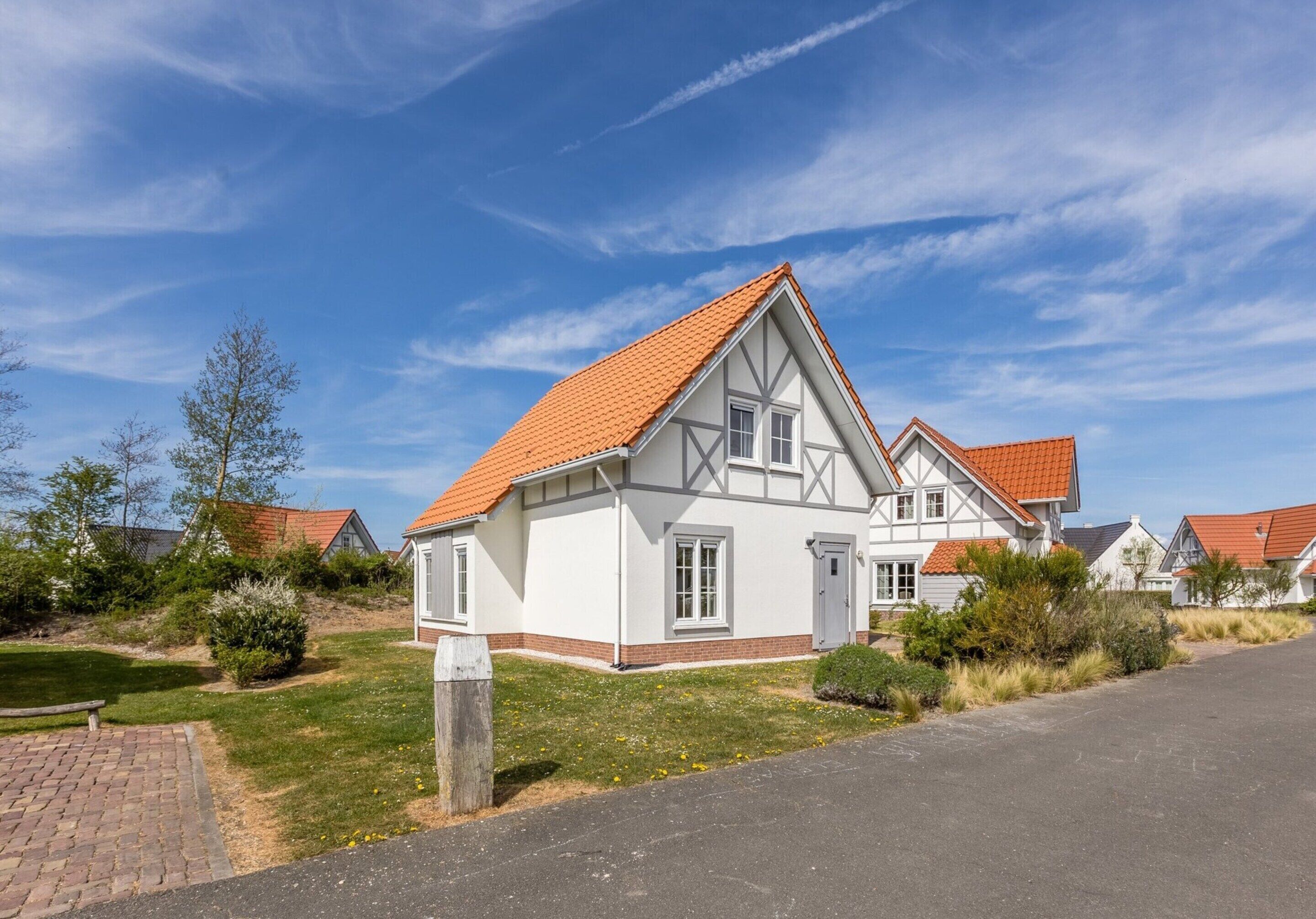 Une maison de style européen traditionnel, avec un toit recouvert de tuiles rouges, des murs blancs et une façade symétrique.