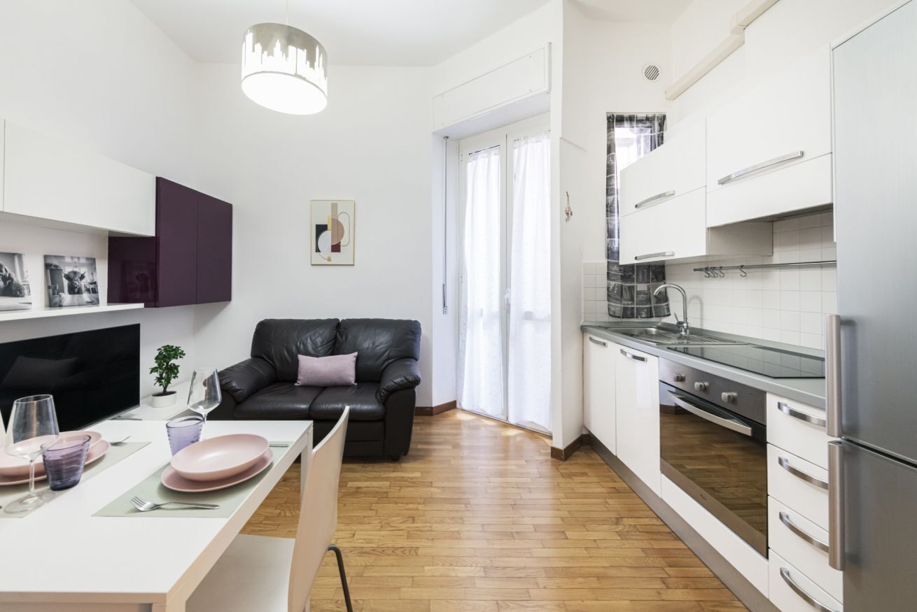 Una cucina moderna con mobili bianchi, un'area pranzo con tavolo apparecchiato per due e un divano in pelle nera.