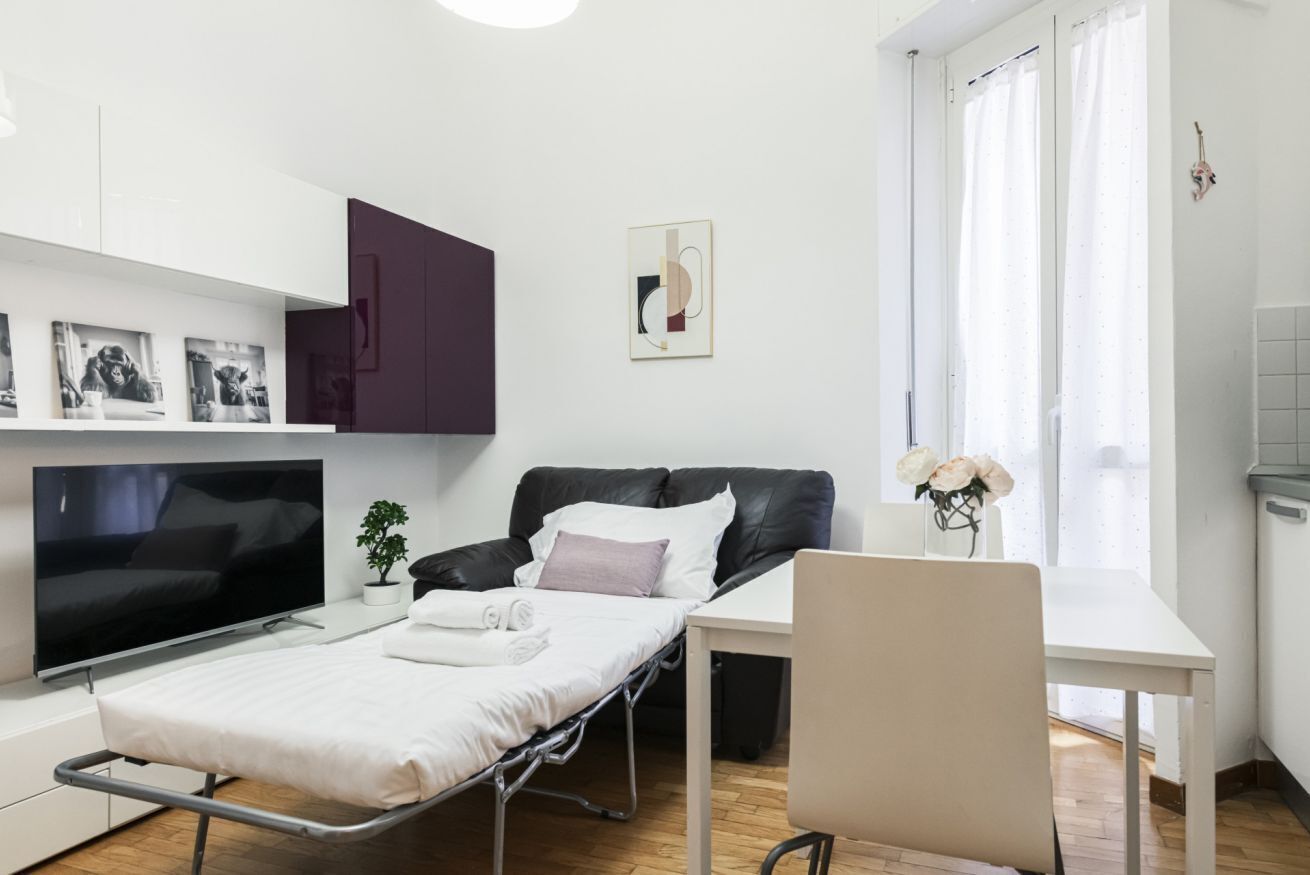 Una camera moderna con un letto, una scrivania, una TV e una finestra con tende.
