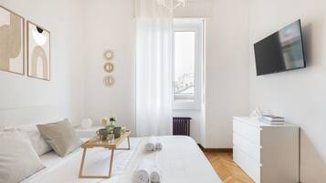Una camera d'albergo con un letto, un comodino con un vassoio, una televisione e vista all'esterno.