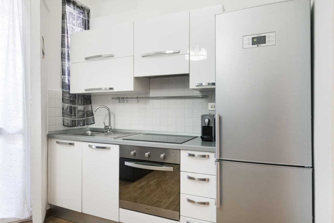 Una cucina moderna con mobili bianchi, elettrodomestici in acciaio inossidabile, forno integrato e frigorifero.