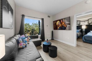 Ett modernt vardagsrum med en grå hörnsoffa, ett stort fönster med gardiner, en tavla med Minions-motiv och ett litet runt bord.