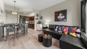 Una sala de estar moderna con un sofá de cuero negro, una mesa de comedor con sillas y una cocina al fondo.