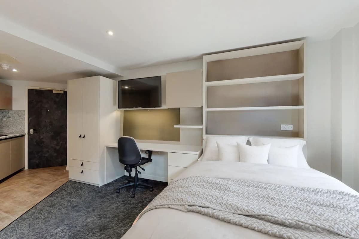 A modern bedroom with a bed, a desk, a chair, and built-in shelving.