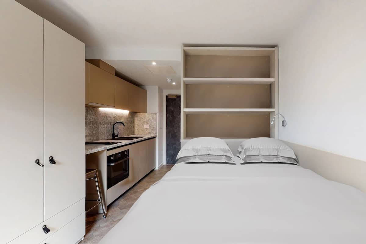 A compact bedroom with a bed, a built-in wardrobe, and a kitchenette.
