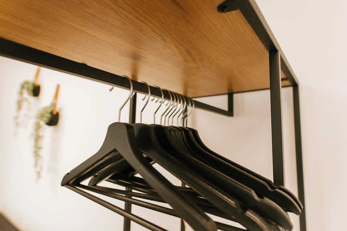 A black hanger rack with multiple hangers against a wooden ceiling.