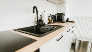 A modern kitchen with a black sink, white cabinets, and a stainless steel trash can. - Staylight City-Loft | private parking | trade fair (Hannover)