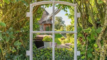 Een rustiek huis met rieten dak, omgeven door weelderig groen en een witte raamkozijn.