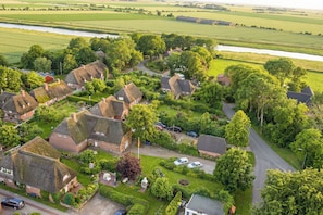 Vue aérienne d’un village rural avec des maisons aux toits de chaume, une rivière et des champs verdoyants.