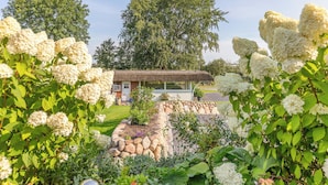 Un bâtiment rustique, doté d’un toit de chaume, entouré d’une végétation luxuriante et de fleurs blanches.