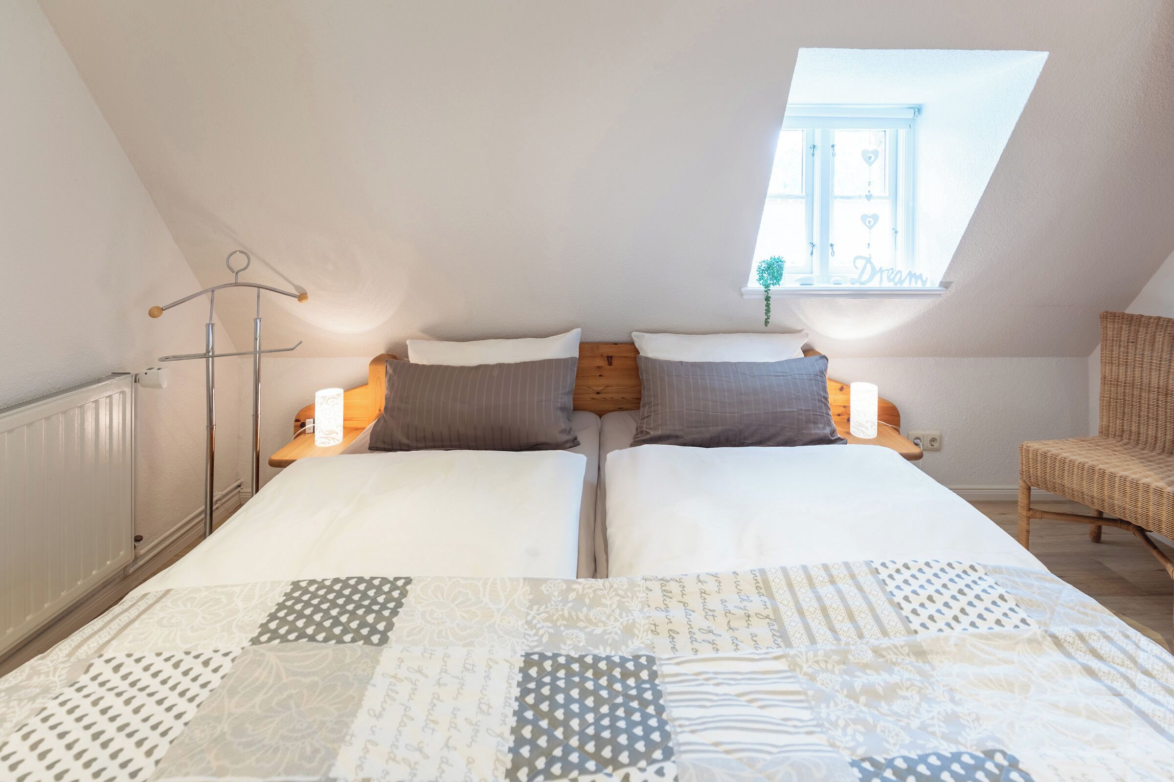 A bedroom with two beds, a skylight, a radiator, and a wicker chair.
