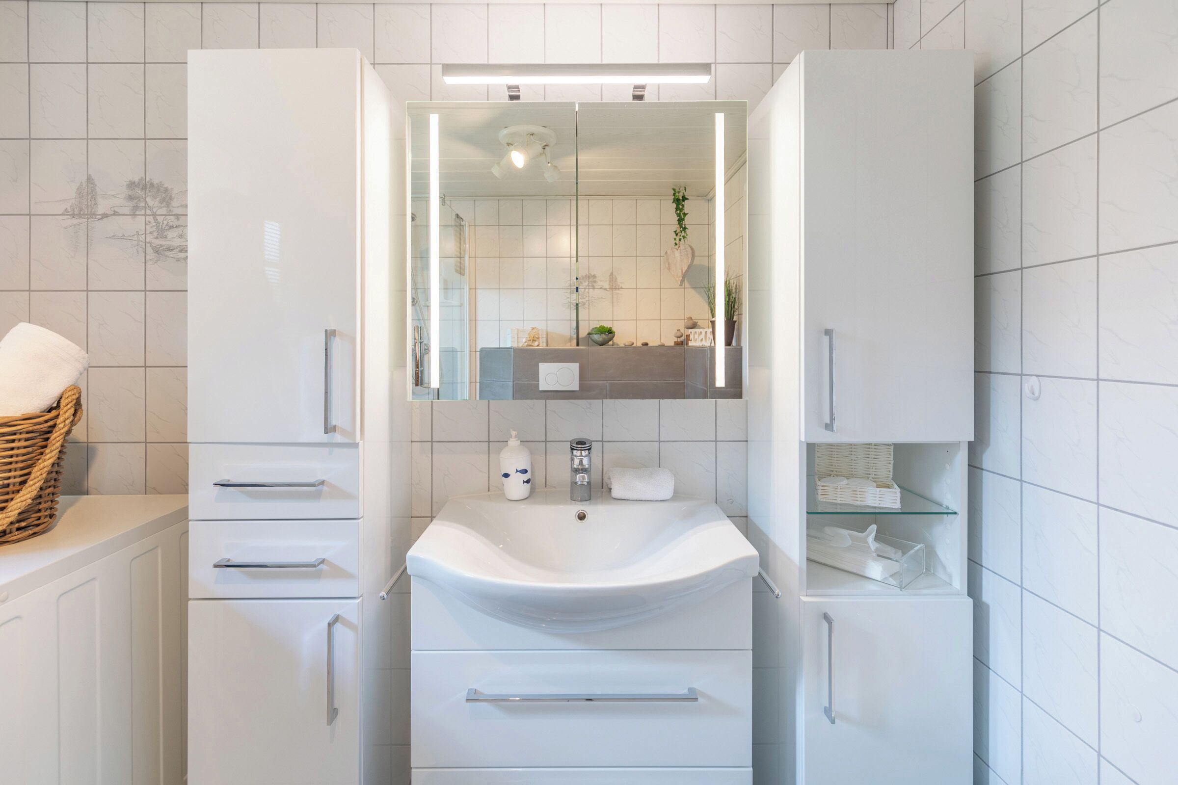 Een moderne badkamer met een witte wastafel, spiegel en kastjes.