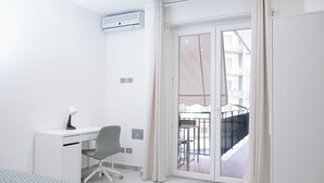 A modern hotel room with a white desk, grey office chair, and a large sliding glass door leading to a balcony. - Adelina House | Quiet and Central Flat near University and Subway (Catania)