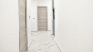 A hallway with a wooden door at the end, white walls, and a marble floor. - Adelina House | Quiet and Central Flat near University and Subway (Catania)