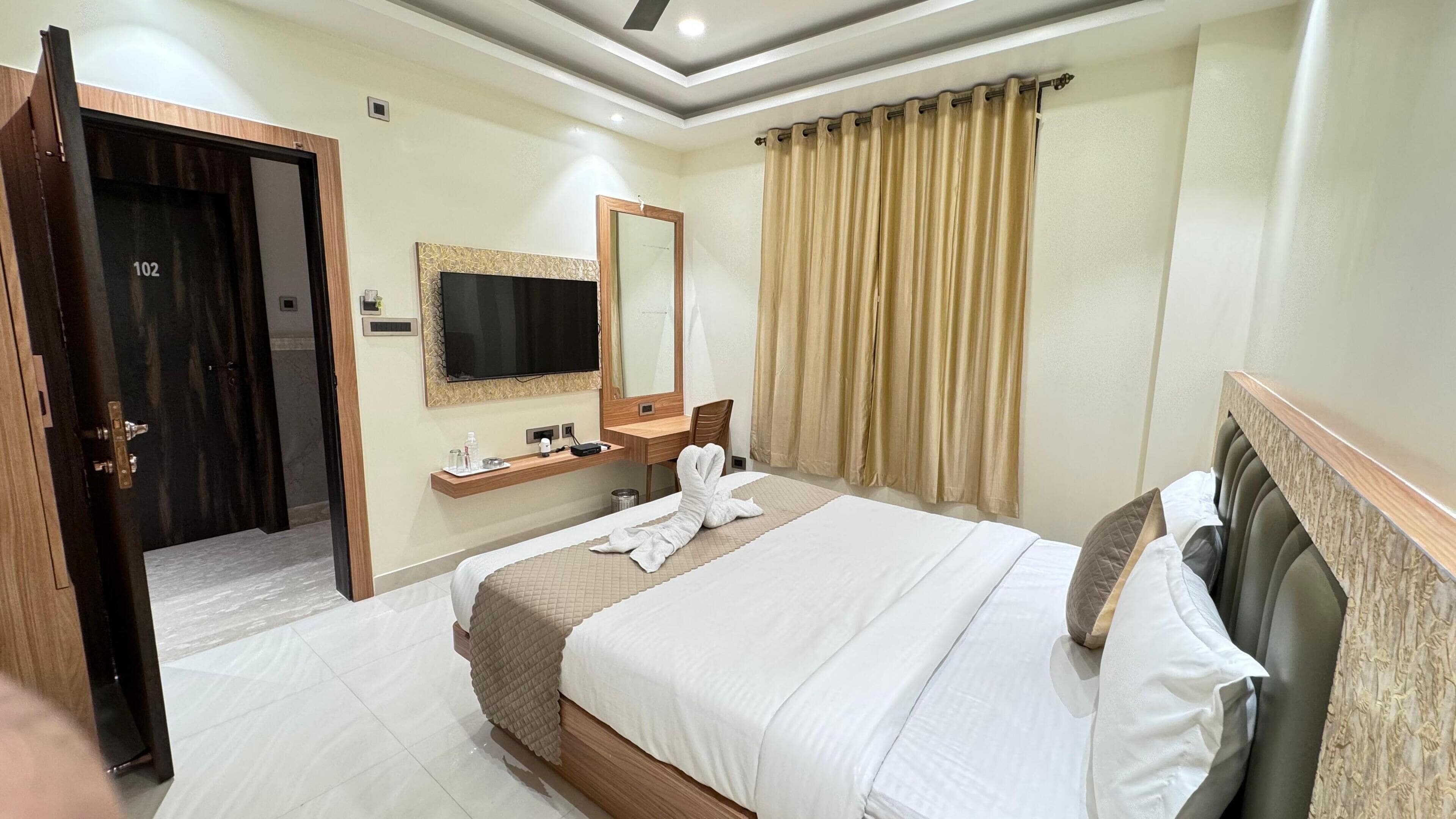 Habitación de hotel con cama, televisión, espejo, escritorio y puerta del baño.