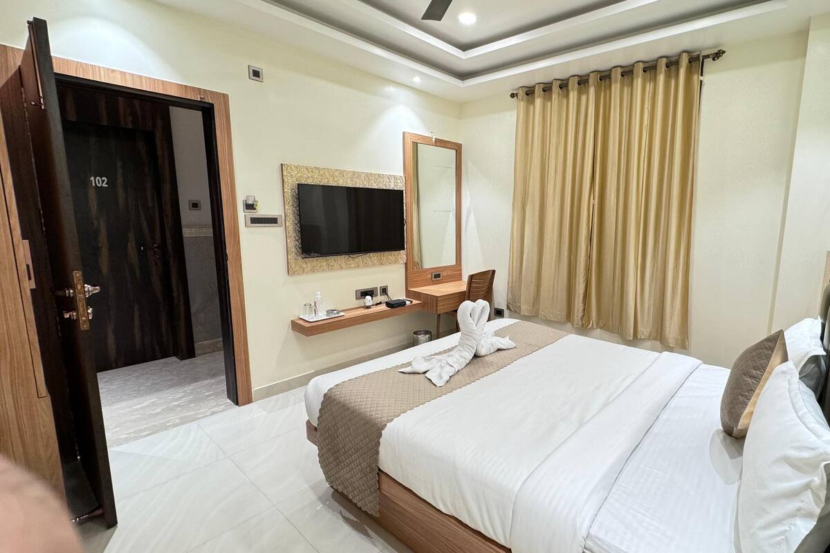 A hotel room with a bed, a TV, a mirror, a desk, and a bathroom door.