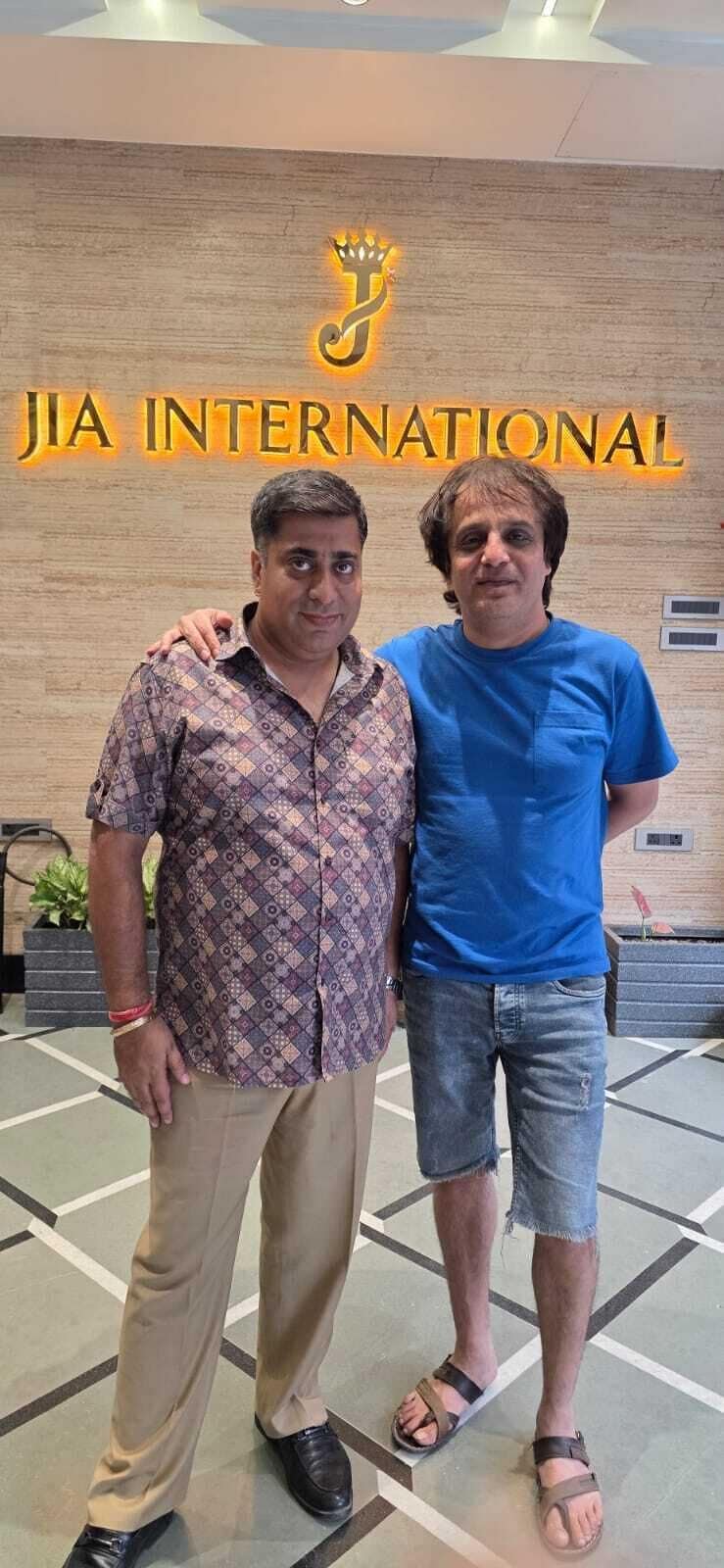 Two individuals standing in a lobby with a sign reading 'JIA INTERNATIONAL' in the background.