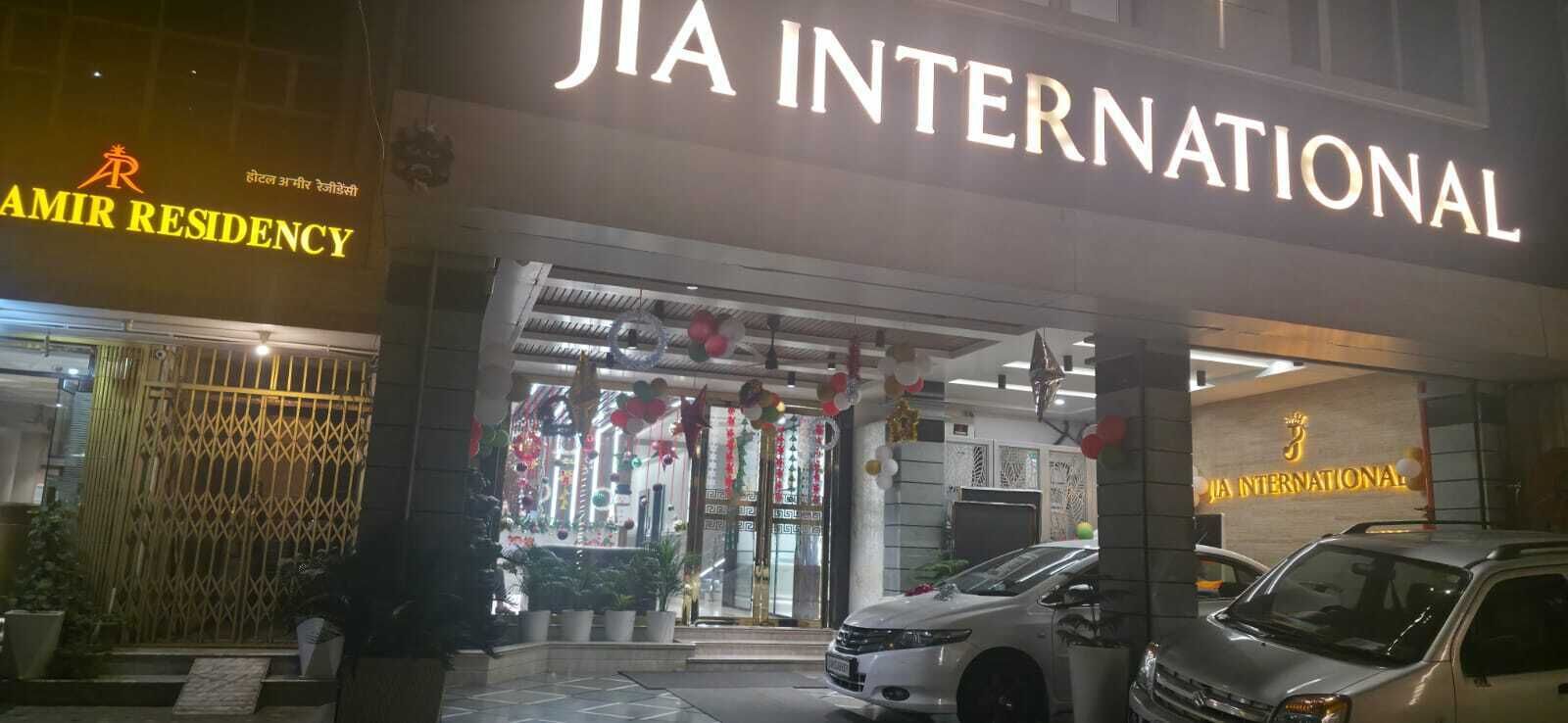 A hotel entrance with a sign for 'JIA INTERNATIONAL' and 'AMIR RESIDENCY'. There are two vehicles parked in front.