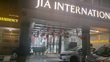 Ein Hotel Eingang mit einem Schild für 'JIA INTERNATIONAL' und 'AMIR RESIDENCY'. Vor dem Eingang stehen zwei Fahrzeuge.