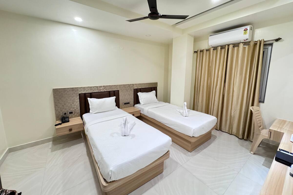 A hotel room with two beds, a desk, a chair, an air conditioning unit, and a ceiling fan.