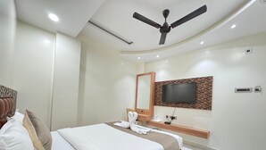A modern hotel room with a bed, a ceiling fan, a TV mounted on the wall, and a small bedside table with a lamp and a bottle. - HOTEL JIA INTERNATIONAL (Patna)