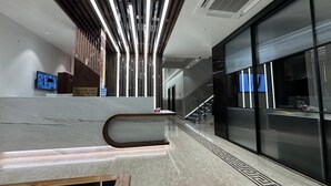 A modern lobby with a marble reception desk, a check-in/out sign, a digital screen, and a staircase leading to upper floors. - HOTEL JIA INTERNATIONAL (Patna)