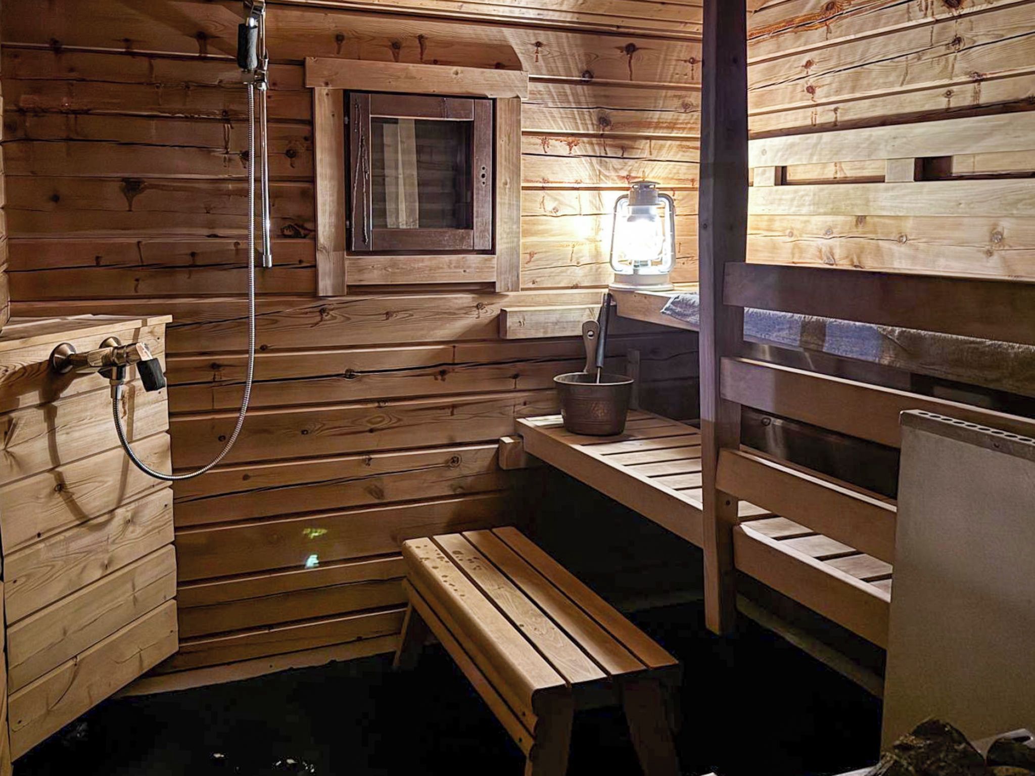 A sauna room with wooden walls, a bench, a small window, and a heater.