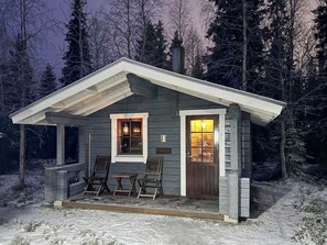 A small cabin with a porch, two chairs, a table, and a lit interior. - Villa taikavuosseli by Interhome (Kuusamo)