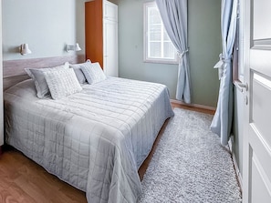 A bedroom with a bed, a nightstand, a window with curtains, and a door. - Villa taikavuosseli by Interhome (Kuusamo)
