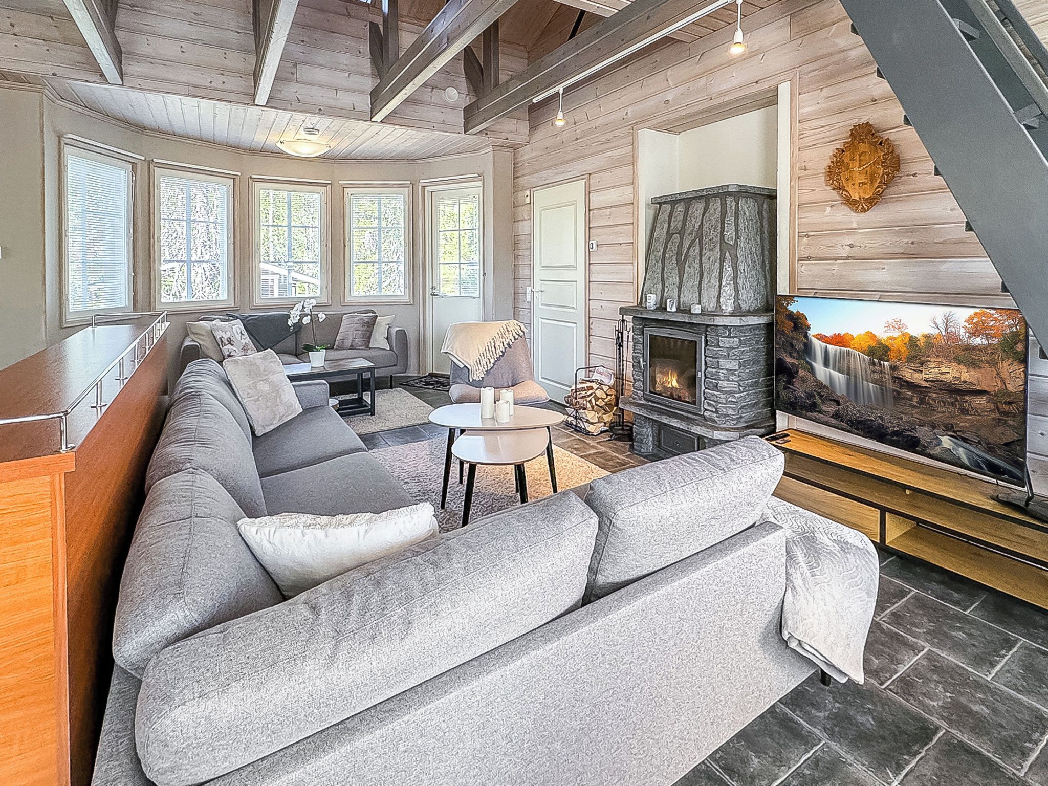 A modern living room with a stone fireplace, large windows, and a sectional sofa.