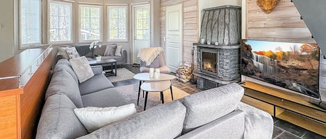 Ein modernes Wohnzimmer mit Kamin aus Stein, großen Fenstern und einem Ecksofa.