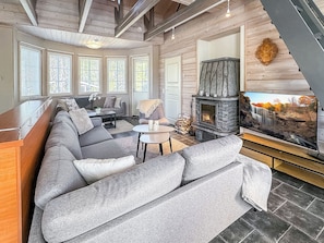 A modern living room with a stone fireplace, large windows, and a sectional sofa. - Villa taikavuosseli by Interhome (Kuusamo)