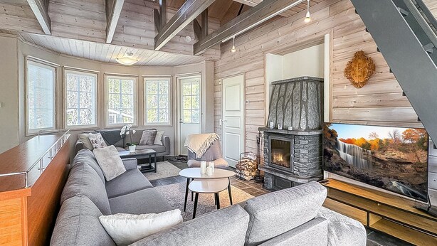 A modern living room with a stone fireplace, a large sofa, and a television displaying a waterfall scene.