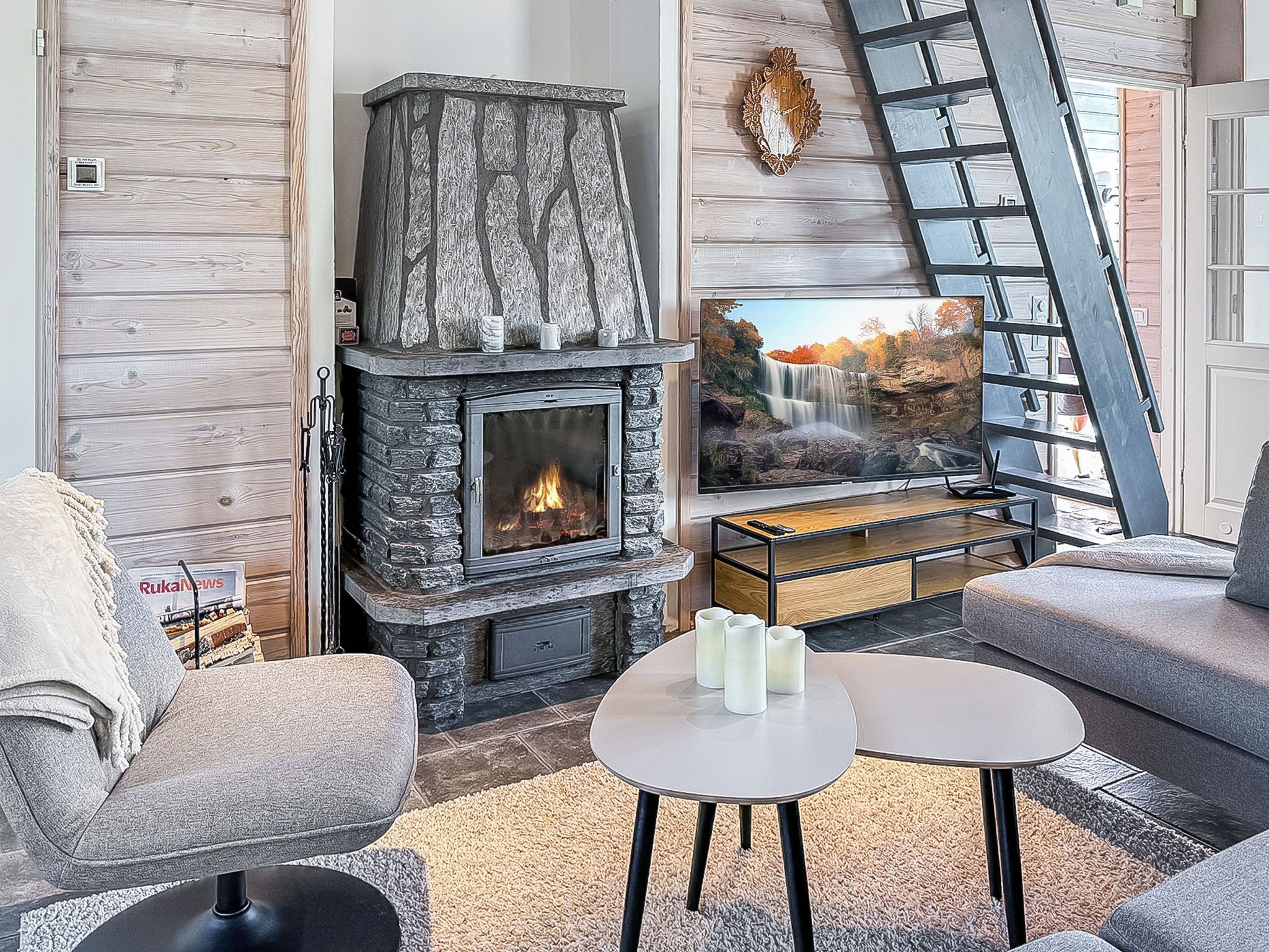 A cozy living room with a stone fireplace, comfortable seating, a coffee table, and a television displaying a scenic waterfall.