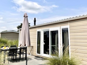 Il s’agit d’un bâtiment d’un seul étage doté d’un patio comprenant une table et des chaises, un parasol et une porte-fenêtre coulissante.