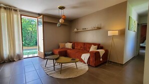 A living room with a sofa, two coffee tables, a lamp, and a view through a glass door.