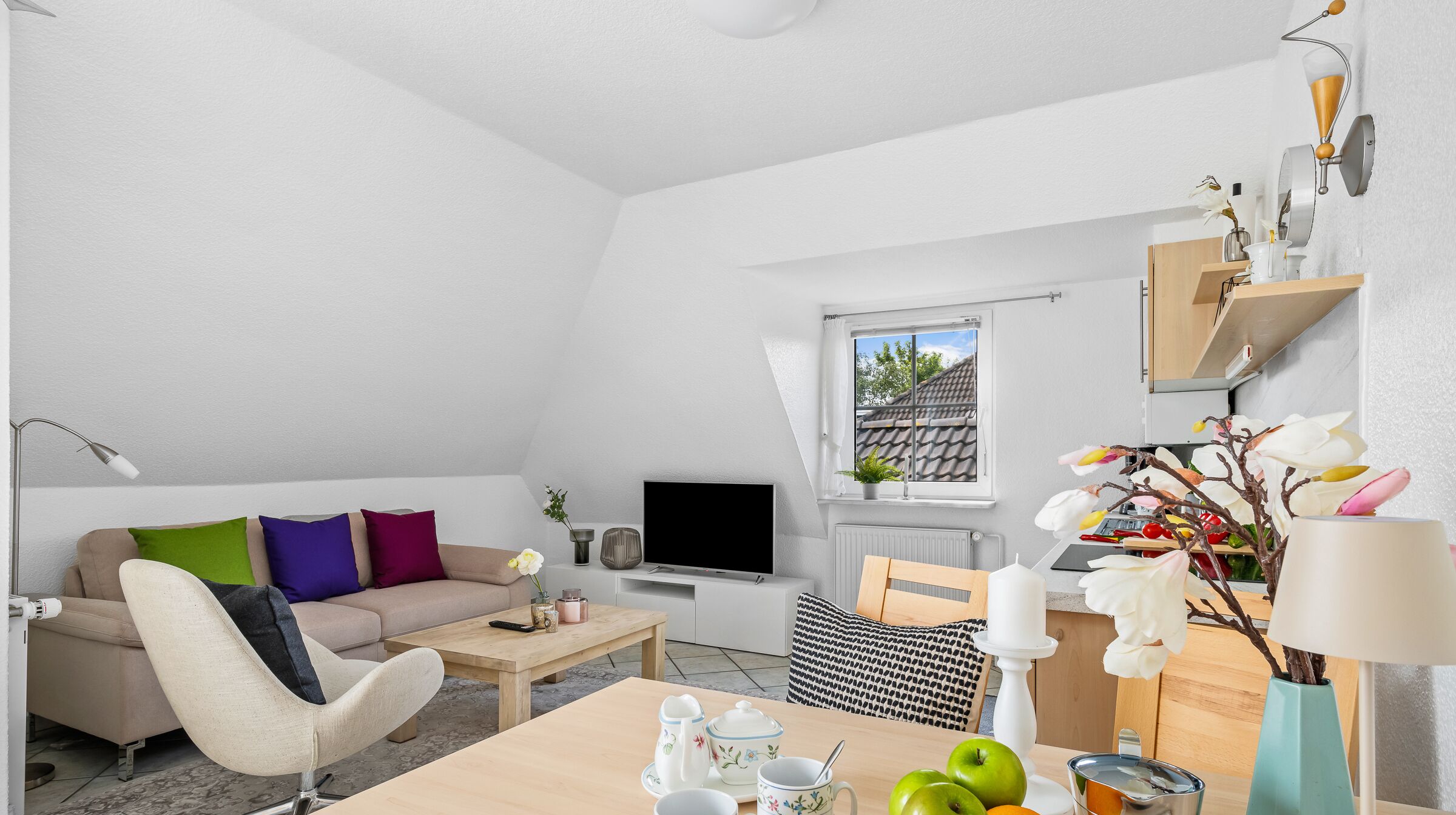 A modern living room with a sofa, coffee table, TV, and a dining area with a table set for tea.