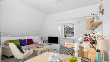 A modern living room with a sofa, coffee table, TV, and a dining area with a table set for tea.