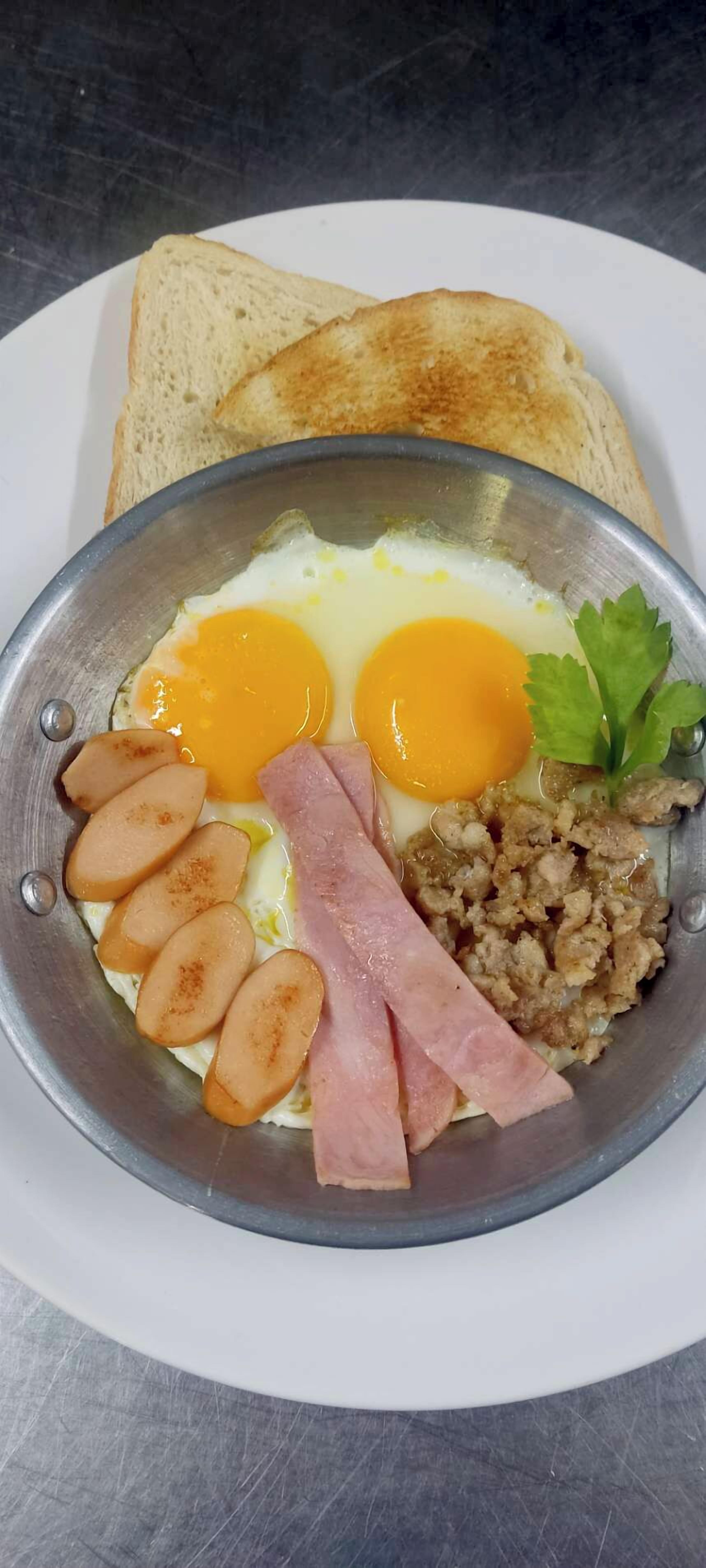 Une assiette de petit-déjeuner comprenant des œufs, du jambon, des saucisses et des toasts.