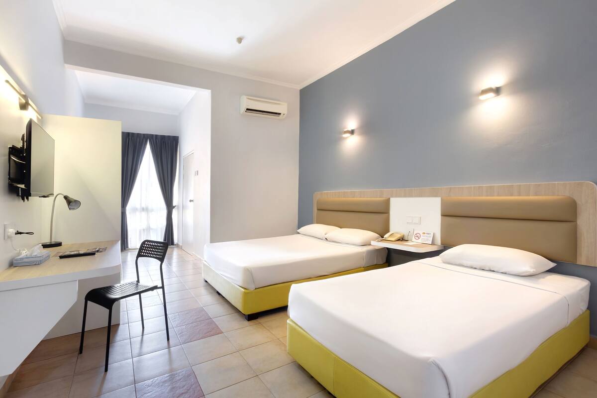 A hotel room with two beds, a desk with a chair, a TV, and a window with curtains.